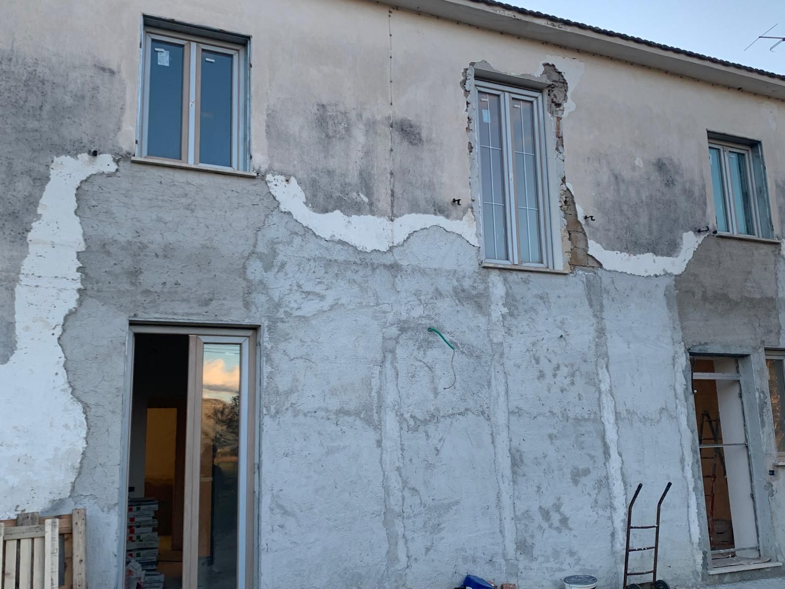 Facciata grigia e deteriorata dell'edificio, con intonaco screpolato, porta aperta e finestre ai piani superiore e inferiore.