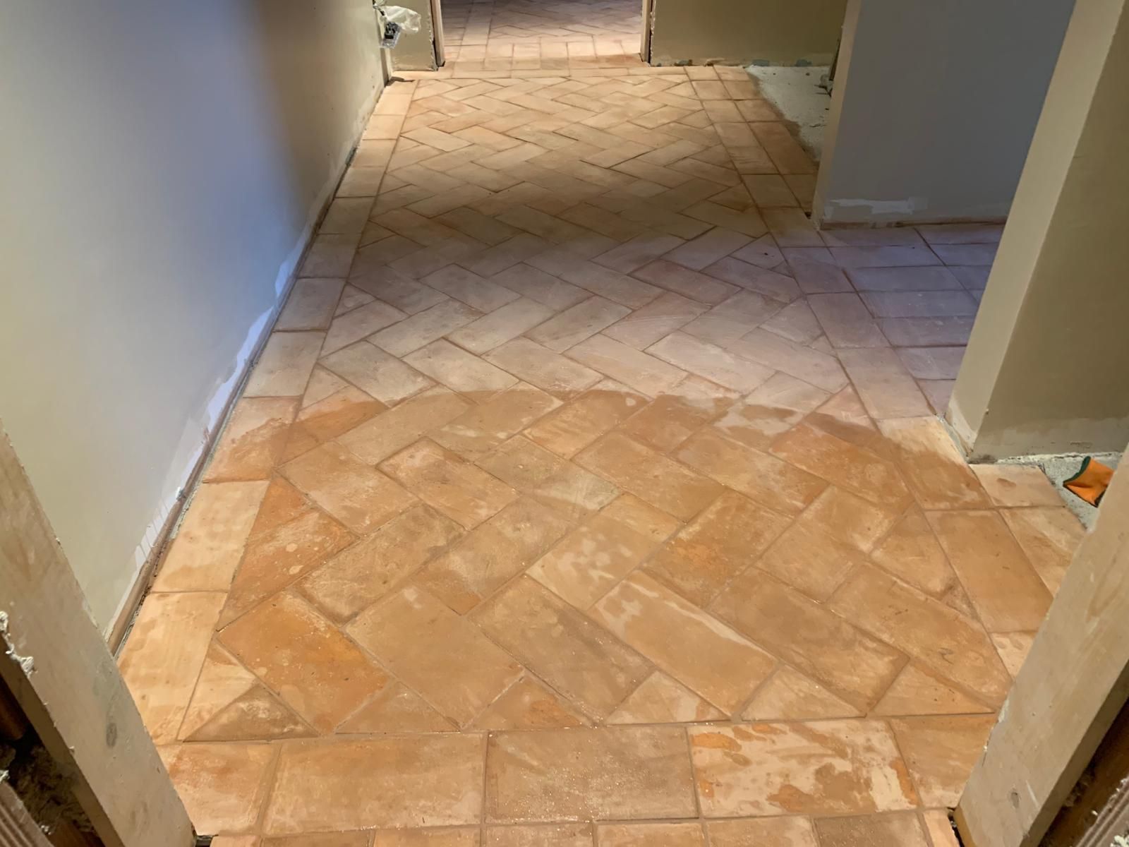 Pavimento del corridoio piastrellato con piastrelle beige e marrone chiaro disposte diagonalmente tra pareti lisce e porte.