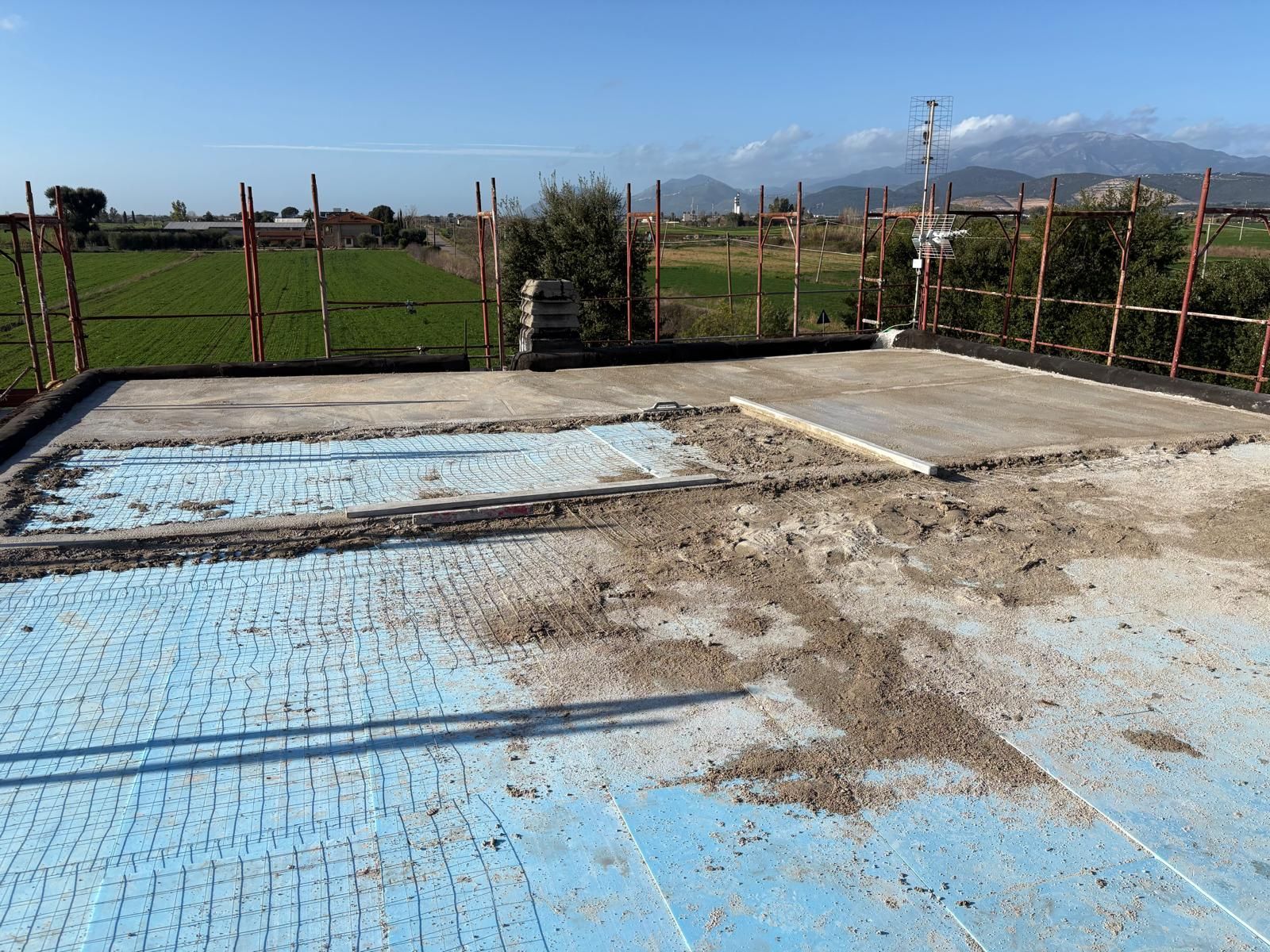 Fondamenta in cemento vuote in costruzione, con isolamento blu e pali di recinzione, in un campo rurale.