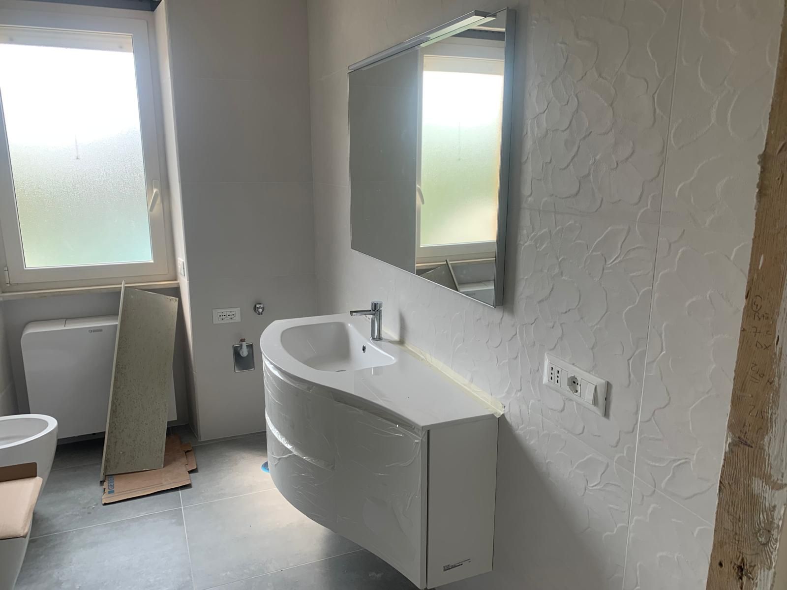 Bagno accessibile con mobile lavabo bianco, specchio, WC e finestra sulla sinistra.