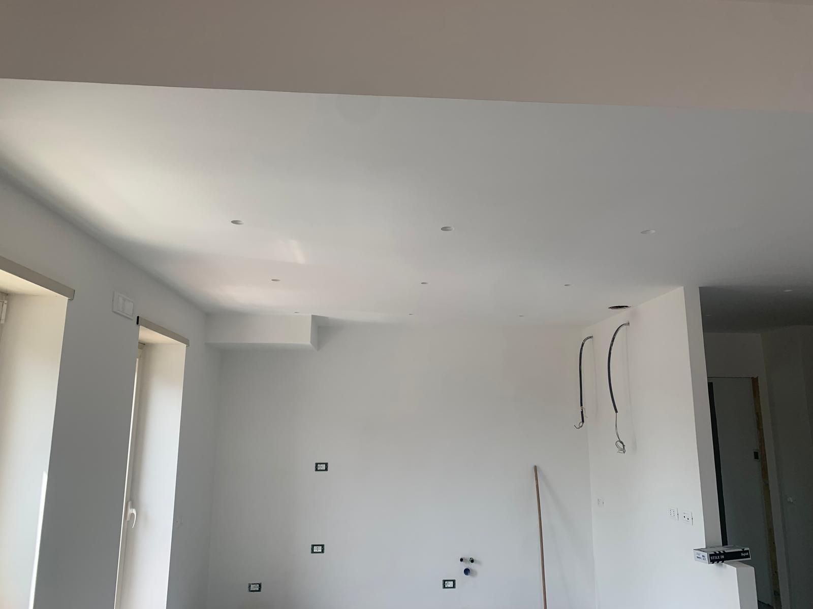 Stanza bianca vuota con pareti non rifinite, luci a soffitto e aperture per porte in costruzione