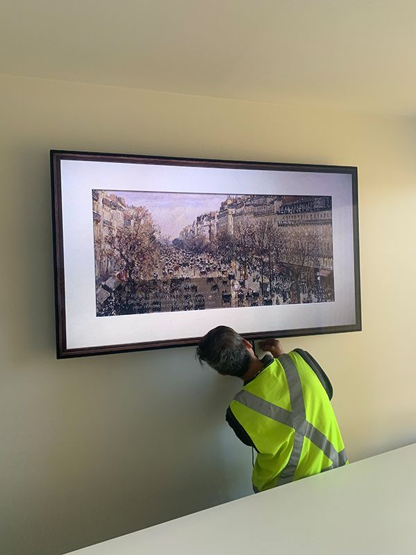 Man In A Yellow Vest Is Hanging A Picture On A Wall — Telecommunication Company In Denman Prospect, ACT