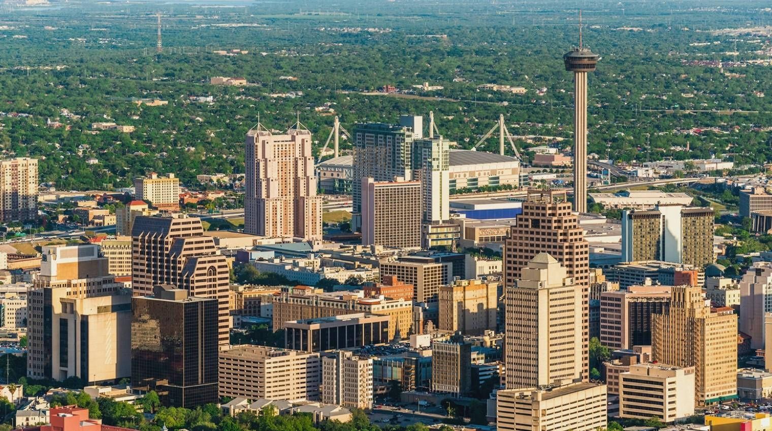 City skyline with tall buildings and a tower above a sprawling green urban landscape