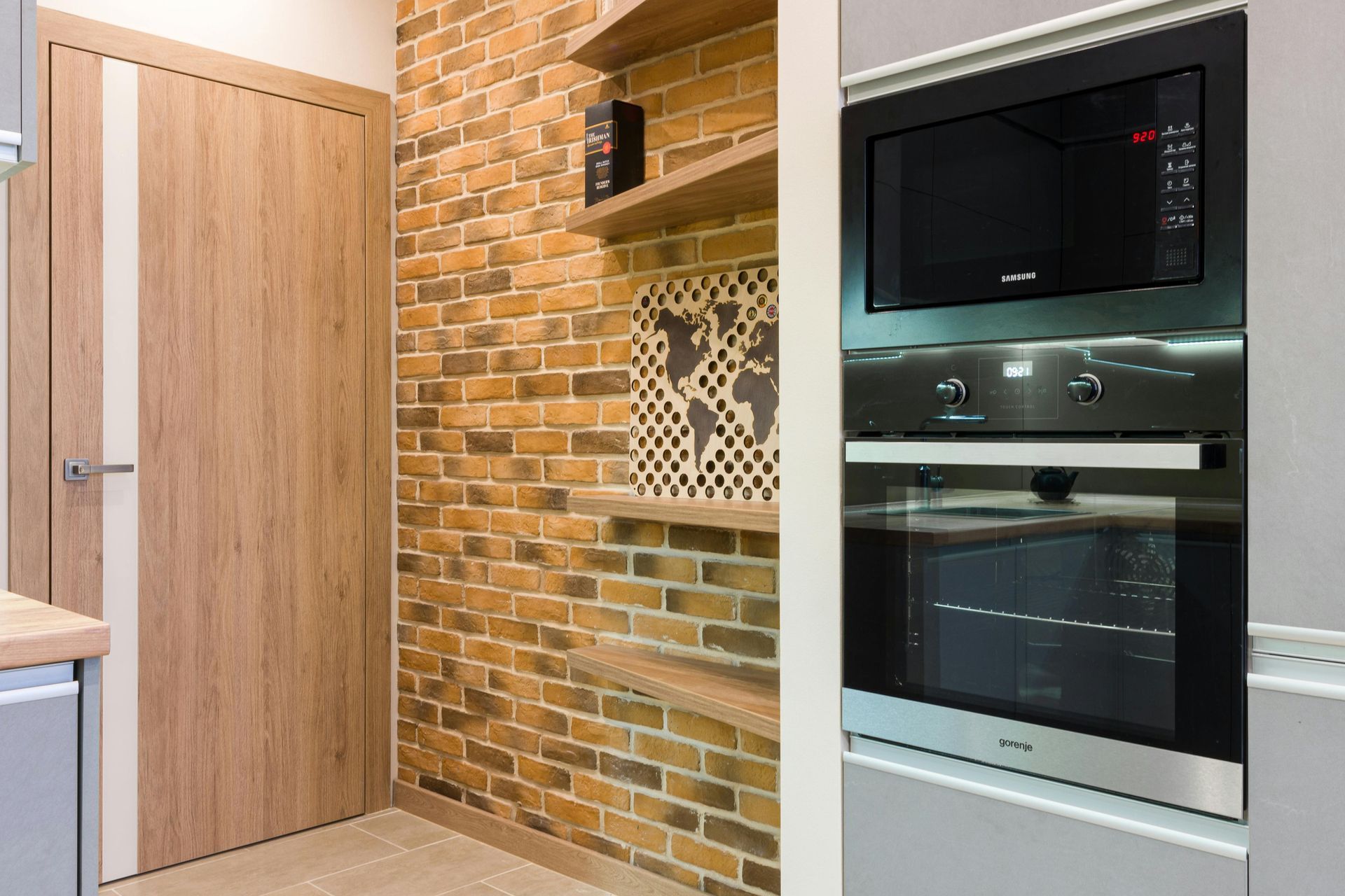 Modern kitchen with wooden door, brick accent wall, and built-in oven and microwave.