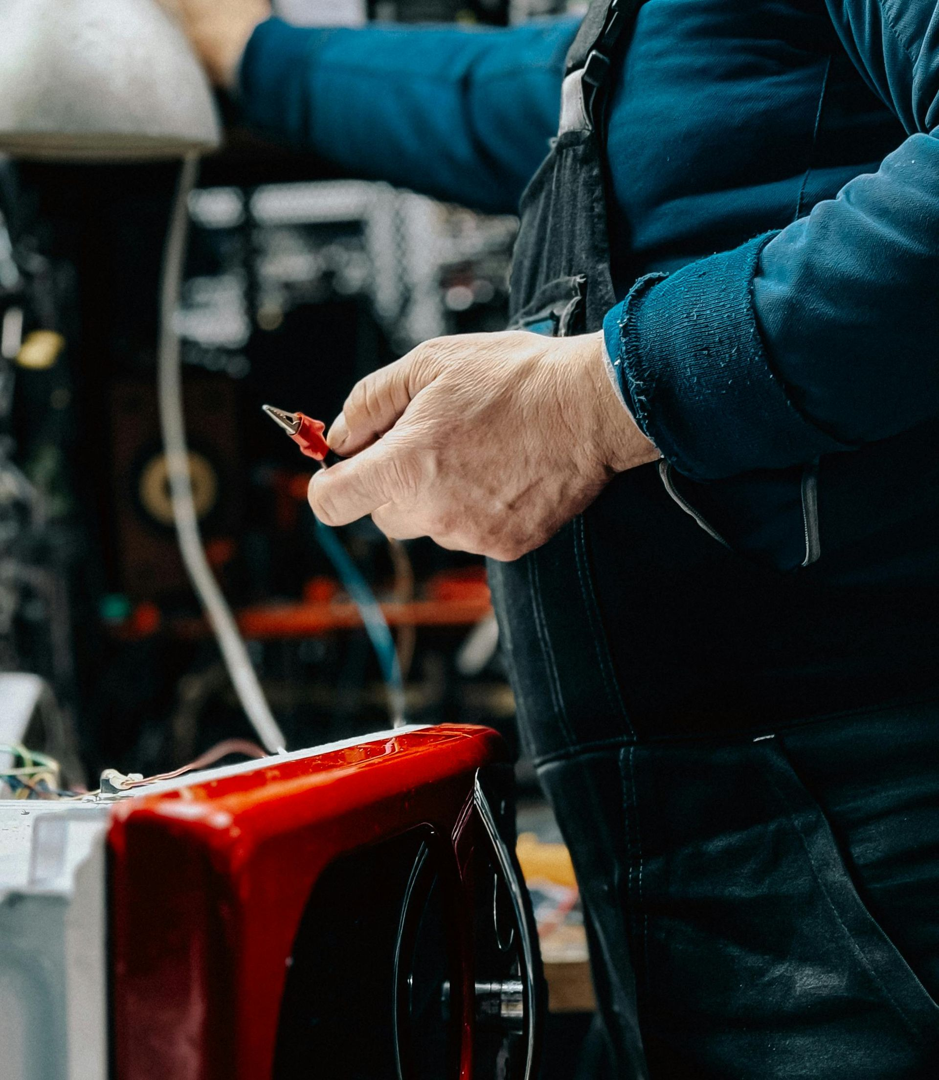 Hand holding a small red piece beside a red machine in a workshop.