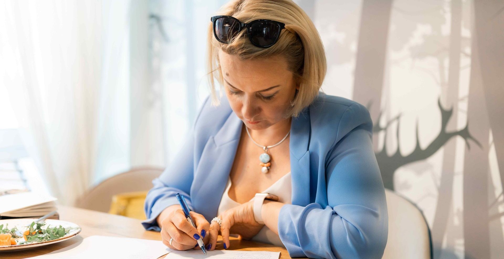 Business Woman Writing Out Micro Narratives for Interview Prep While Eating at Table