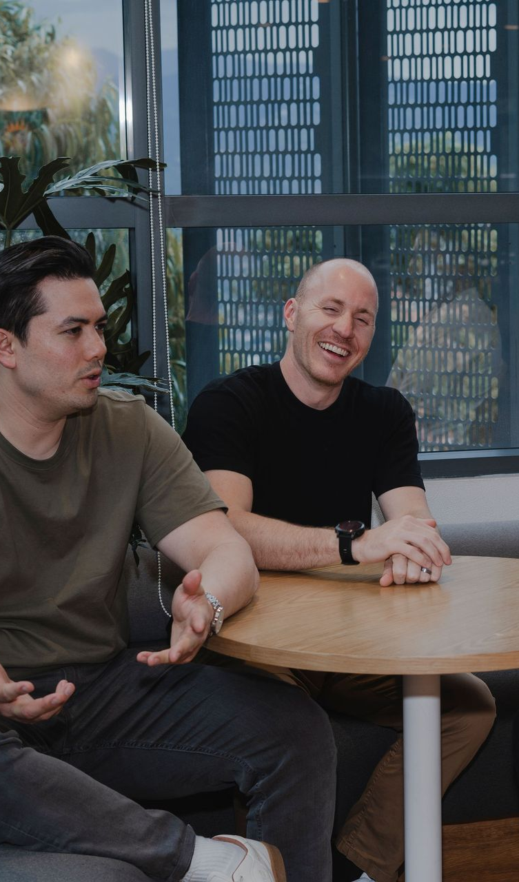 Adam Broda Career Coach and Founder at Broda Coaching, at a table; laughing. Modern office setting with large windows.