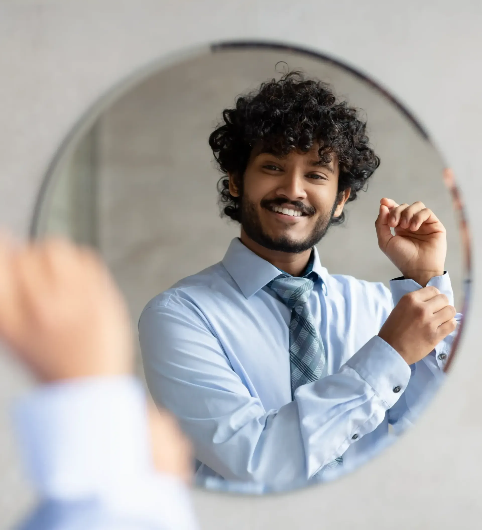 A man in a blue shirt and tie is standing in front of a mirror as he prepares for interview using Broda Coaching method.