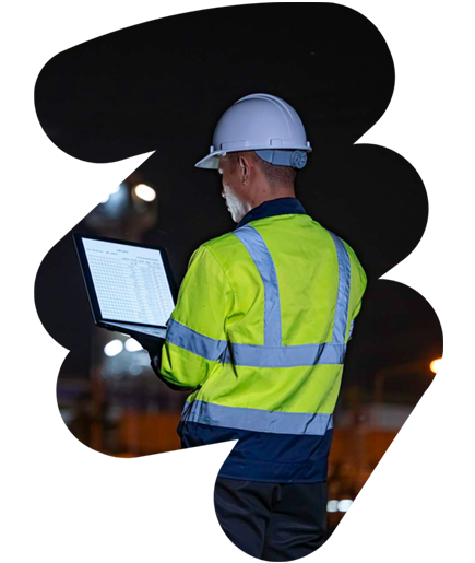 Engineer in hard hat using a laptop at a construction site at night