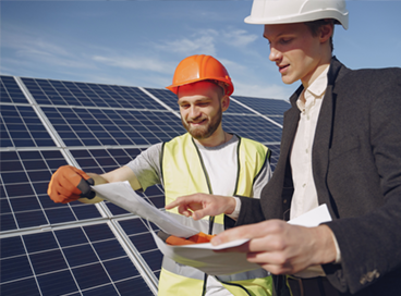 Two engineers reviewing plans beside solar panels on a sunny rooftop