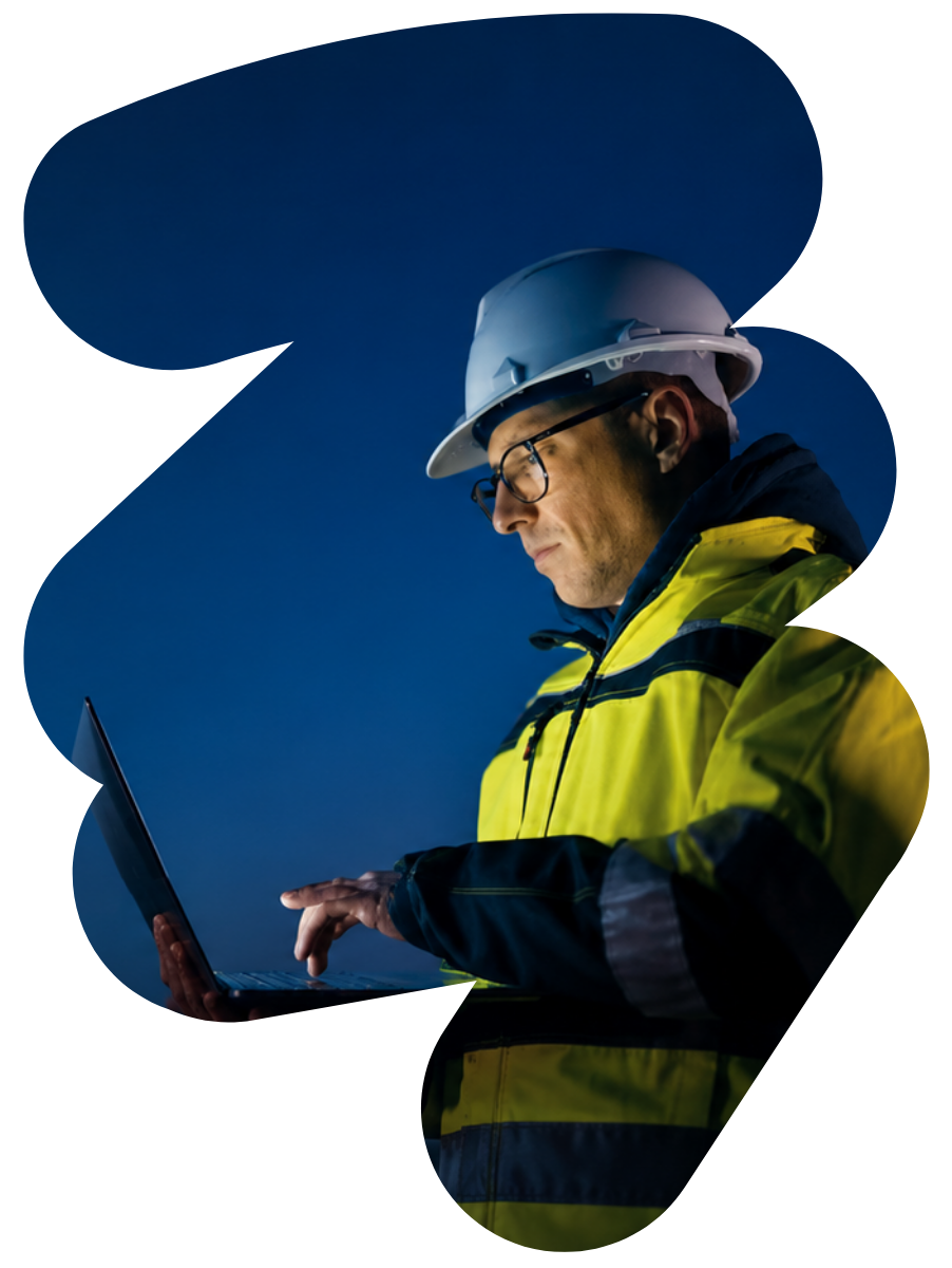 Worker in hard hat and yellow jacket using a laptop against a dark blue background