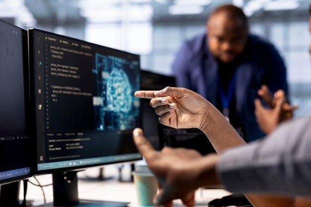 Hands pointing at code and a blue interface on a desktop monitor in a collaborative office setting