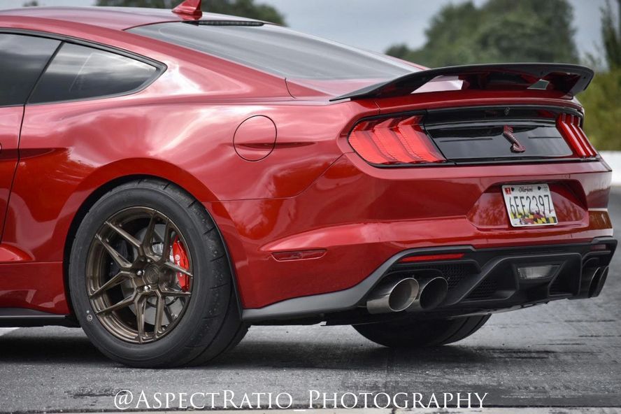 A red mustang is parked on the side of the road.