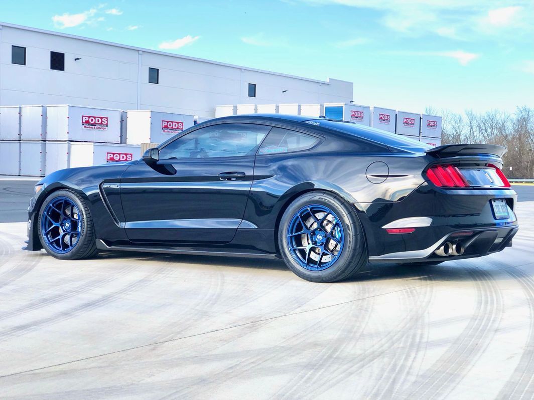 A black ford mustang with blue wheels is parked in front of a building.