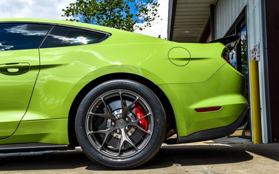 A green mustang is parked in front of a garage.