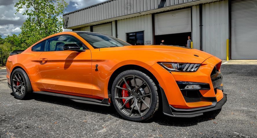 An orange ford mustang is parked in front of a building.