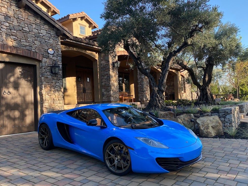 A blue sports car is parked in front of a stone house.