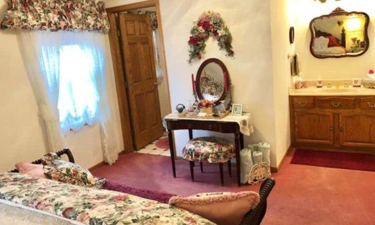 A bedroom with a bed , vanity , mirror and sink.