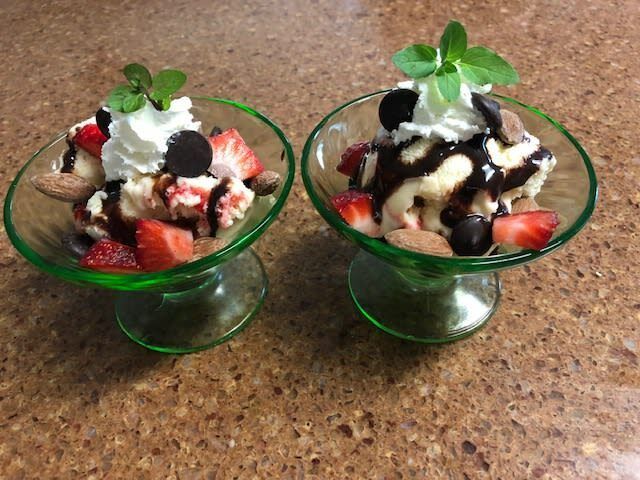 Two bowls of ice cream with strawberries whipped cream and chocolate sauce