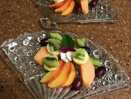 Two fan shaped plates filled with fruit and whipped cream on a table.