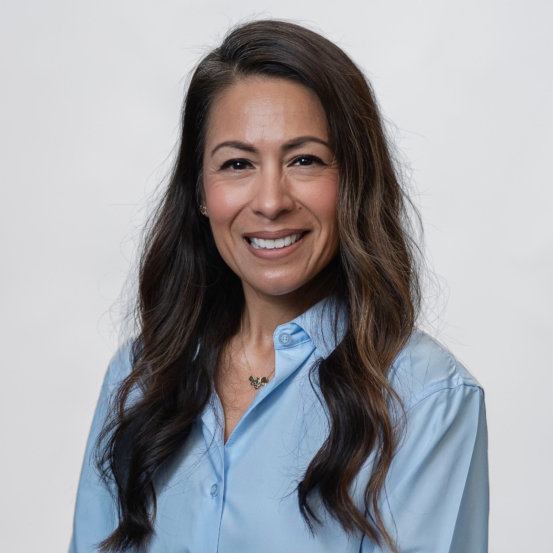 Smiling woman in a light blue shirt against a plain gray background