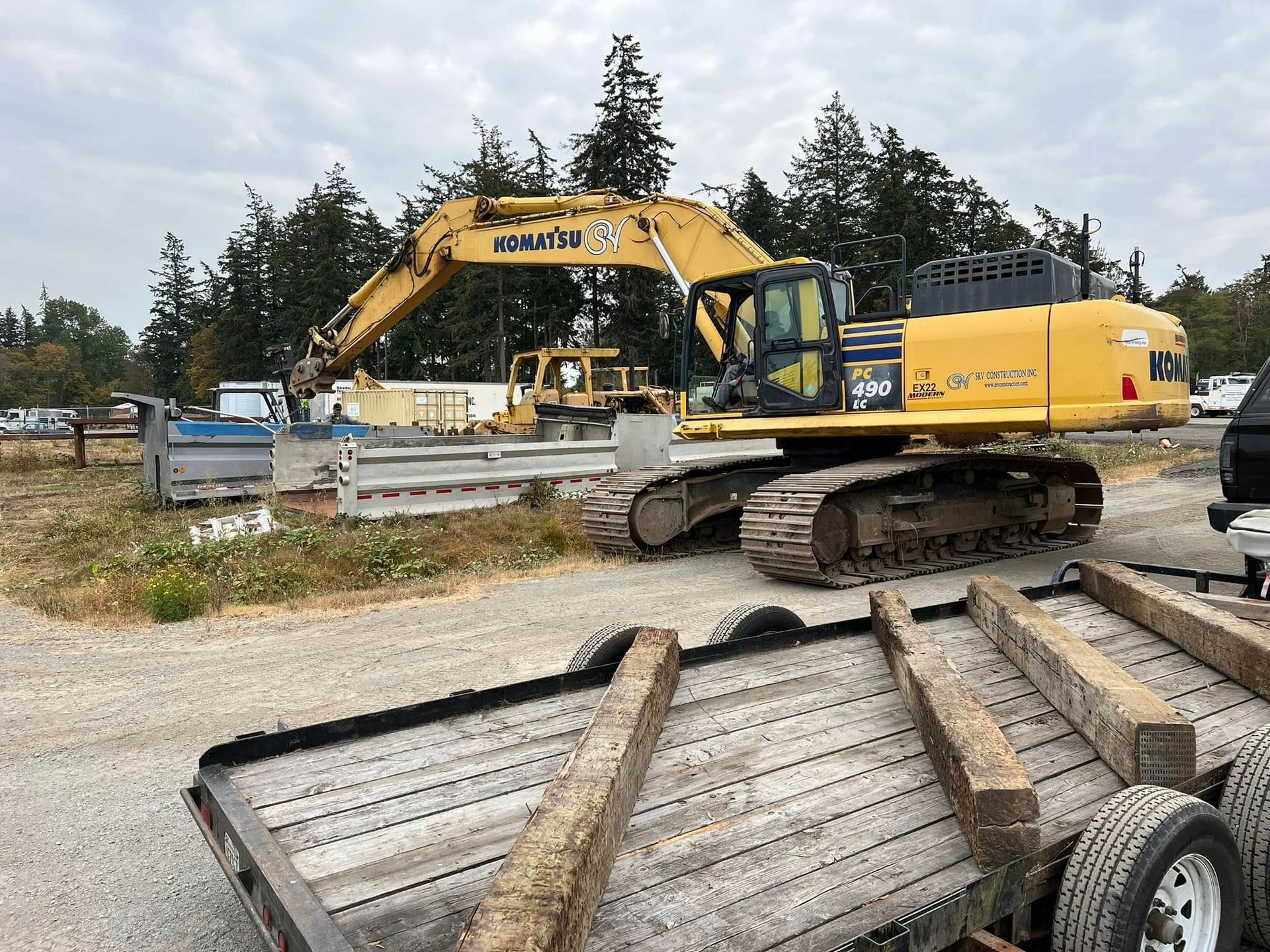 Yellow excavators and a flatbed trailer at a construction site with trees in the background.