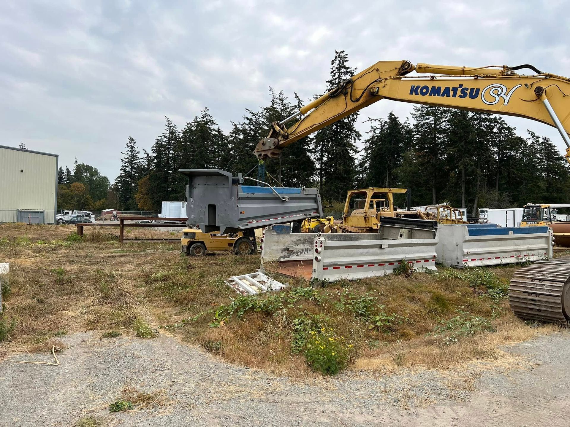 Excavator loading a dump truck at a construction site with concrete barriers and gravel.