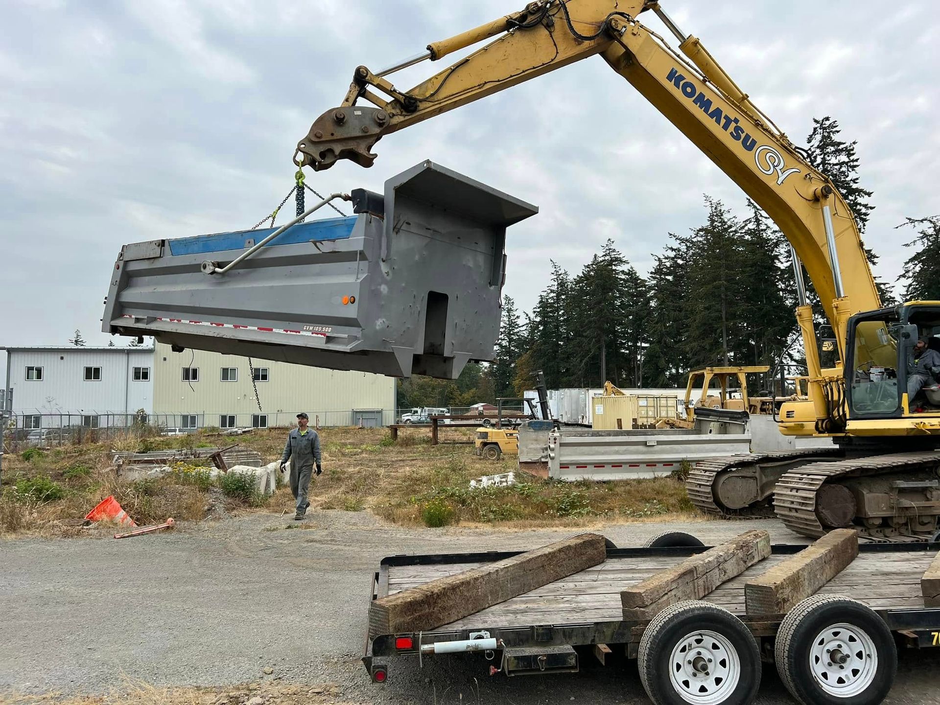 Yellow excavator lifting a gray modular building section at a construction site