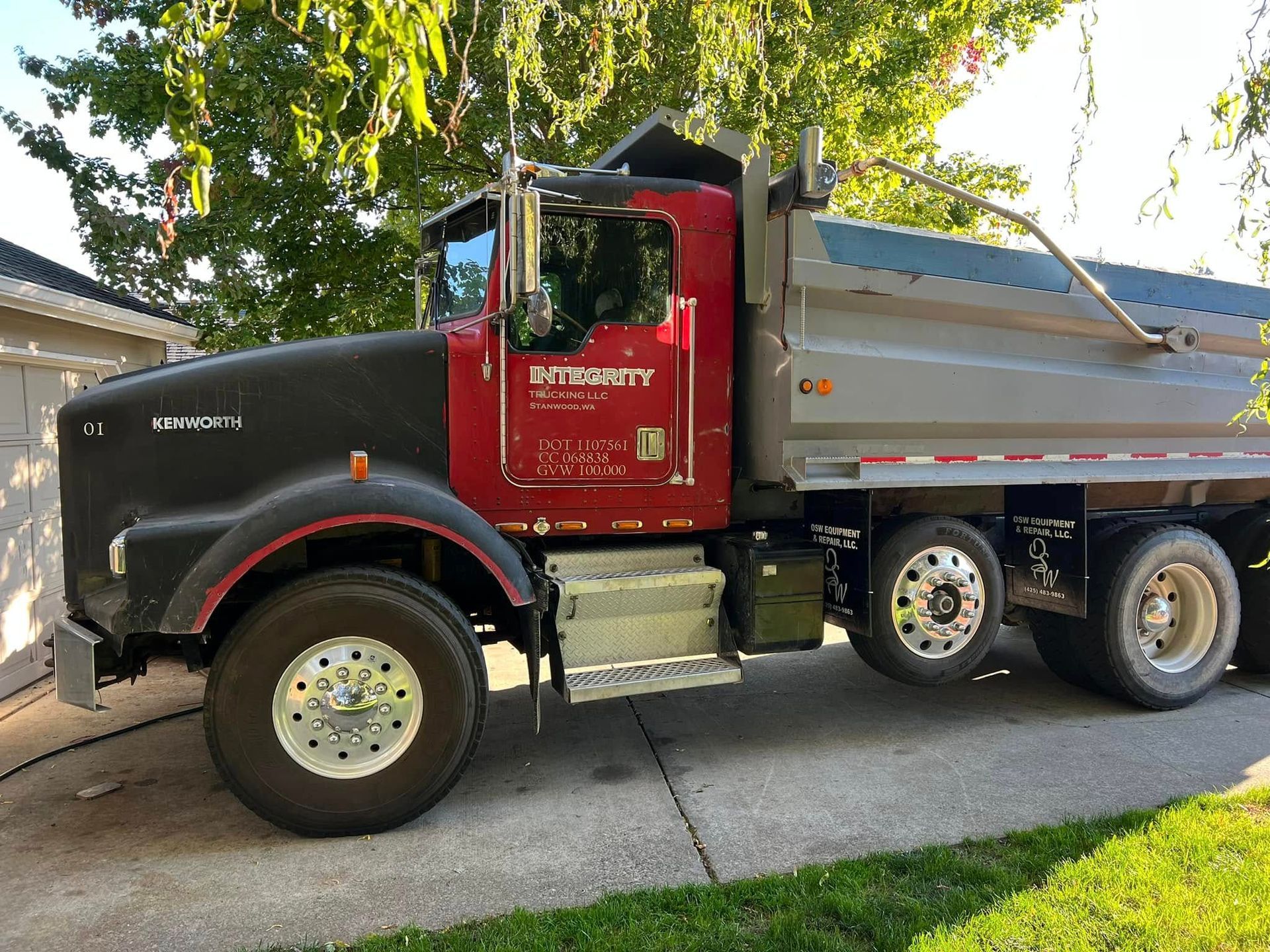 Black and red Peterbilt dump truck parked in a driveway under trees