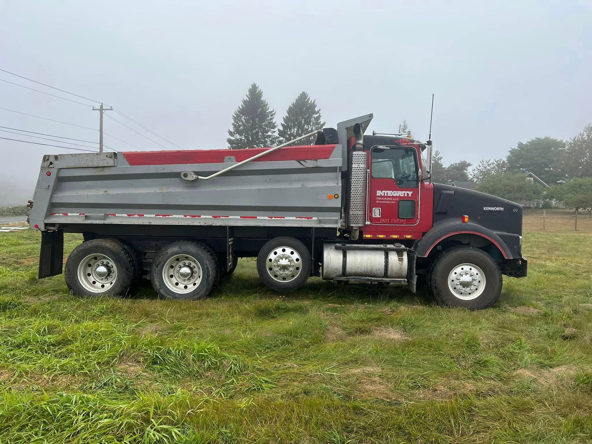 Red and black dump truck parked on a grassy field in light fog