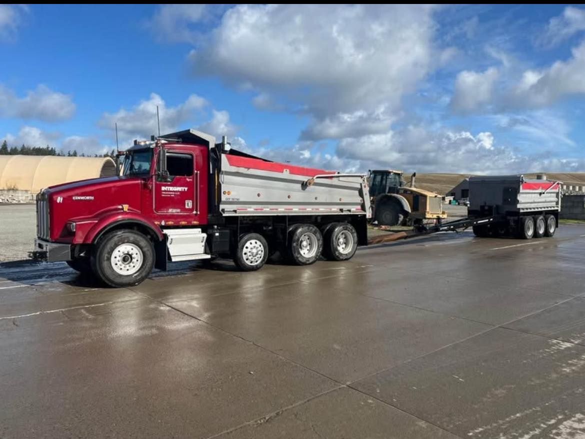 Red dump truck with a trailer on a wet roadway under a cloudy sky