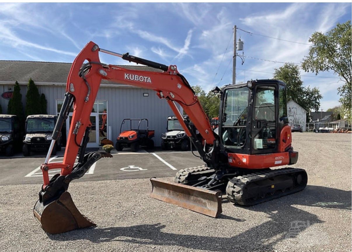 Orange compact excavator with front blade parked on gravel lot outside a building