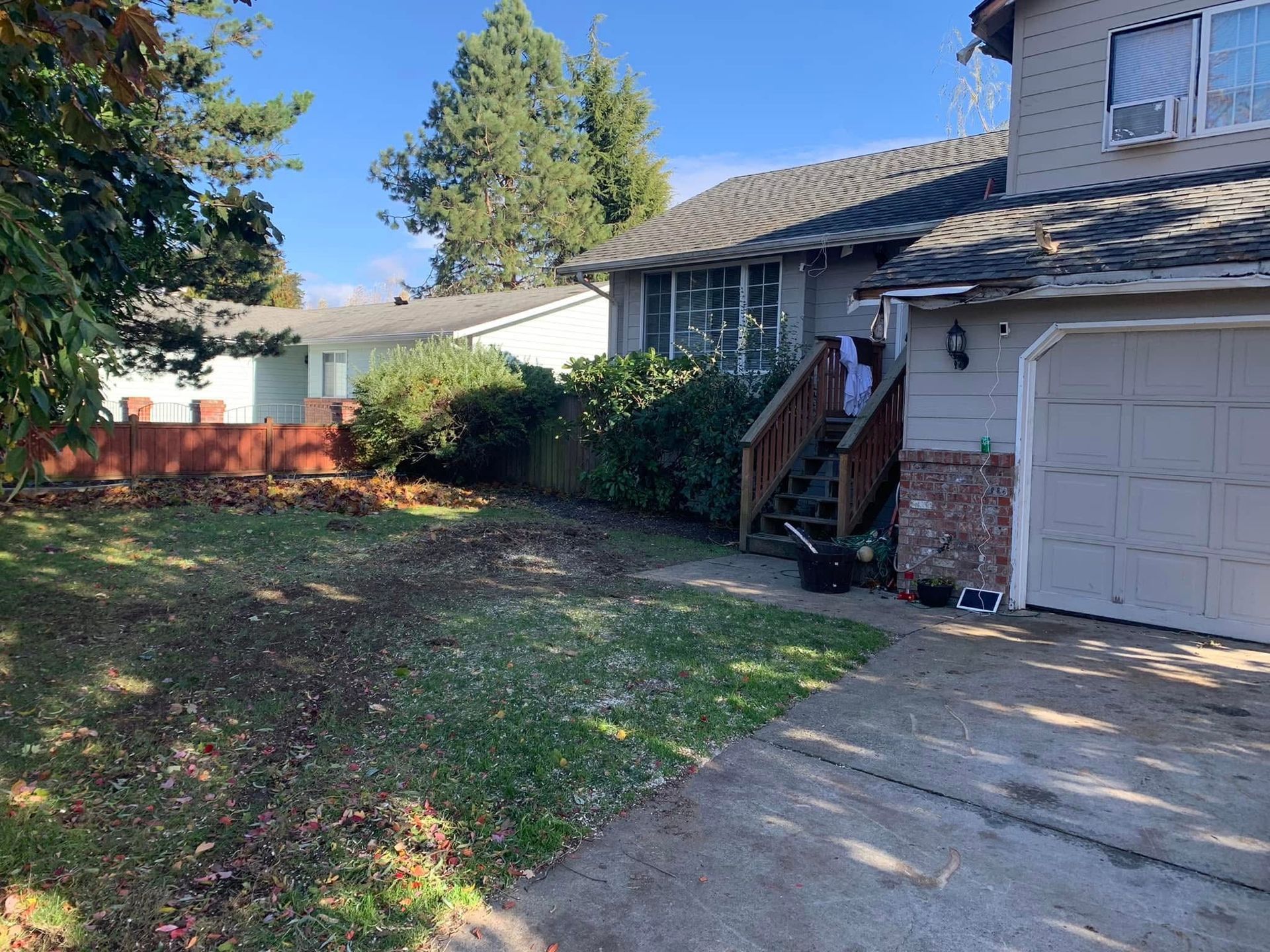 Suburban house with garage, front steps, driveway, and shaded lawn by a wooden fence.