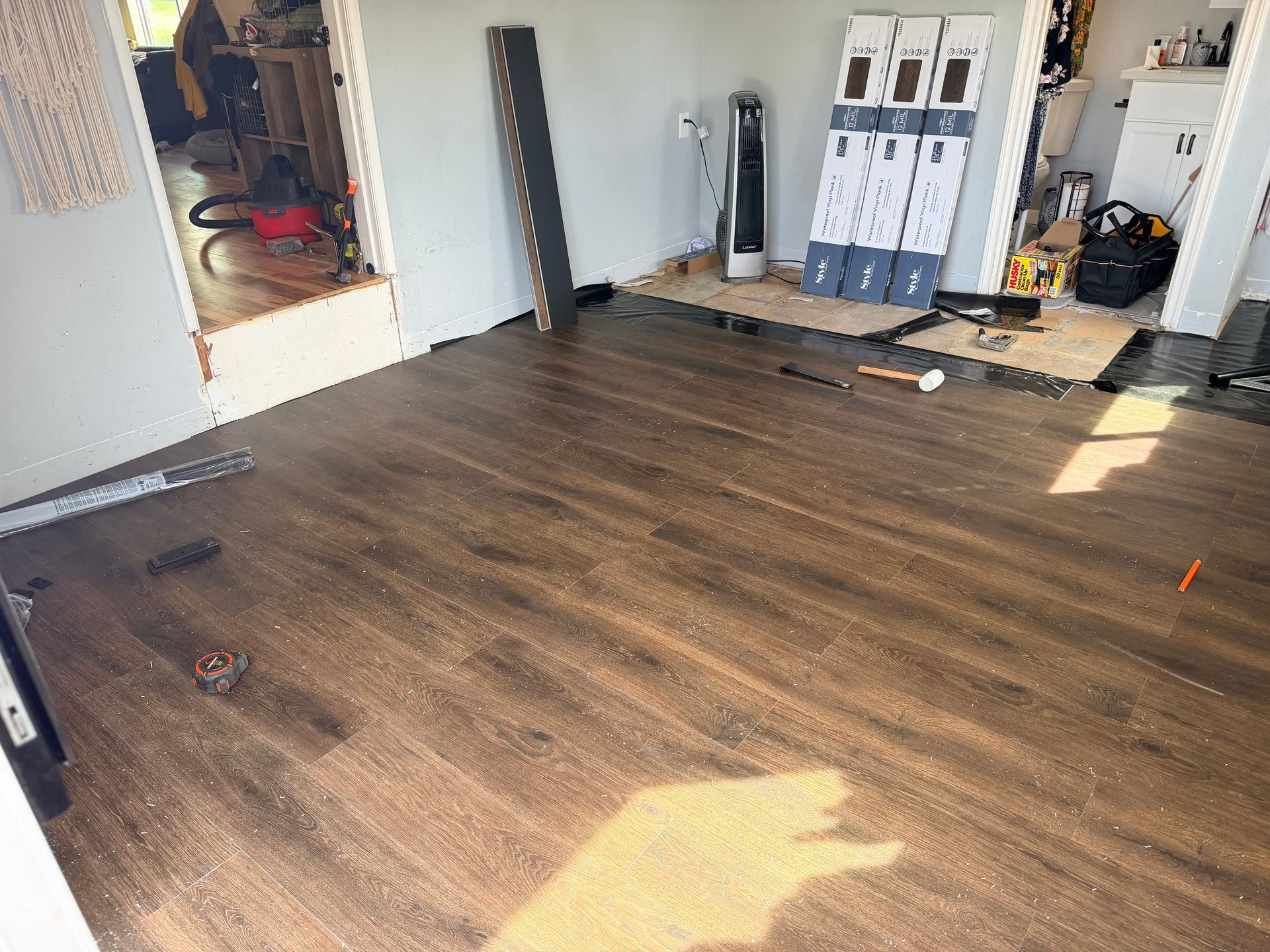 Empty room with dark wood flooring, open doorway, and stacked boxes along the back wall.