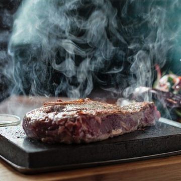 Un steak est en train d'être cuit sur une pierre d'où sort de la fumée.