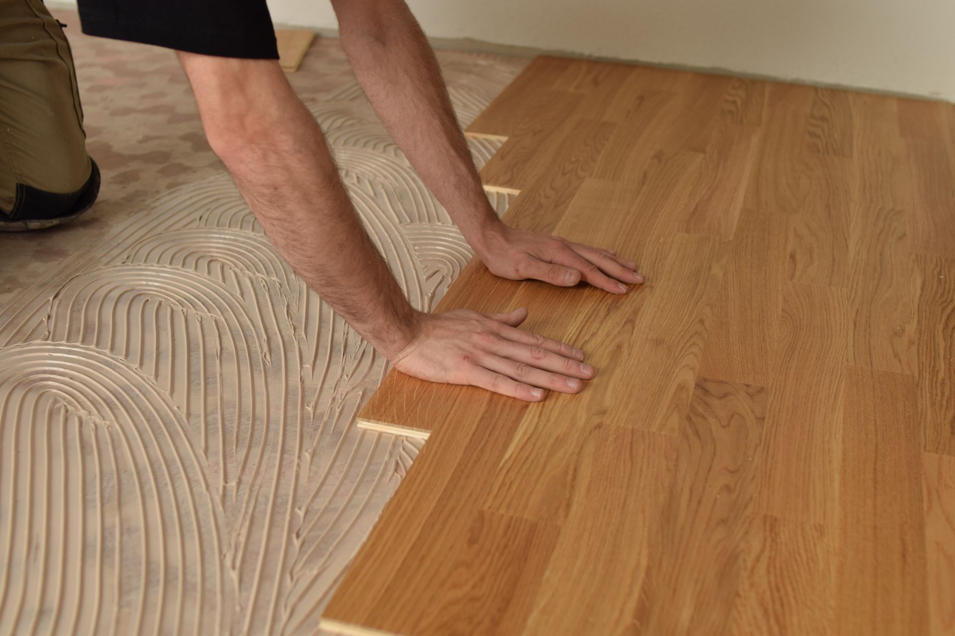 Person kneeling and smoothing a wood floor beside a carpet seam