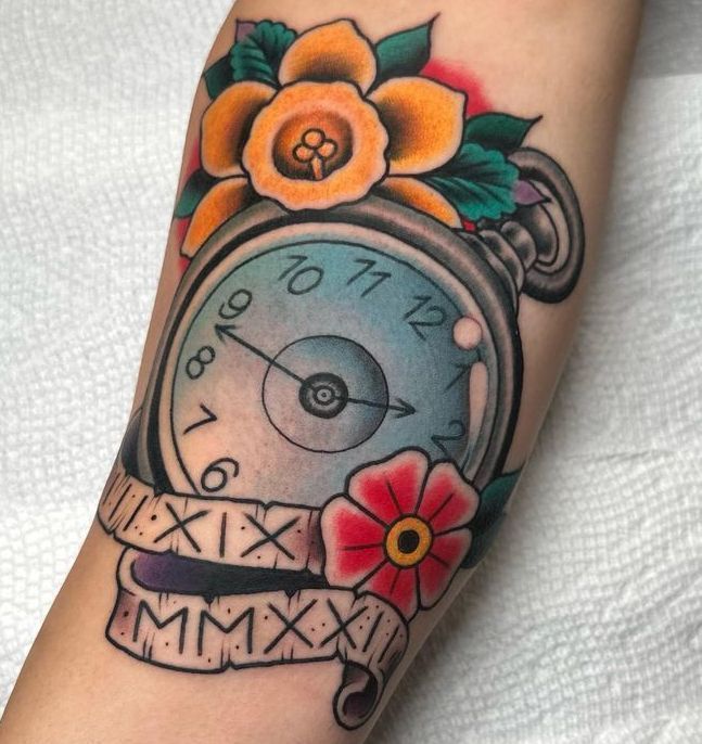 Colorful forearm tattoo of a clock with orange flowers, green leaves, and Roman numerals on a ribbon ribbon band