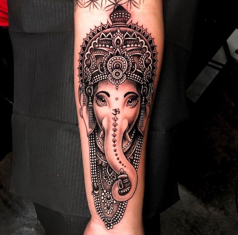 Black-and-gray Ganesha tattoo on a forearm with ornate headdress and detailed linework