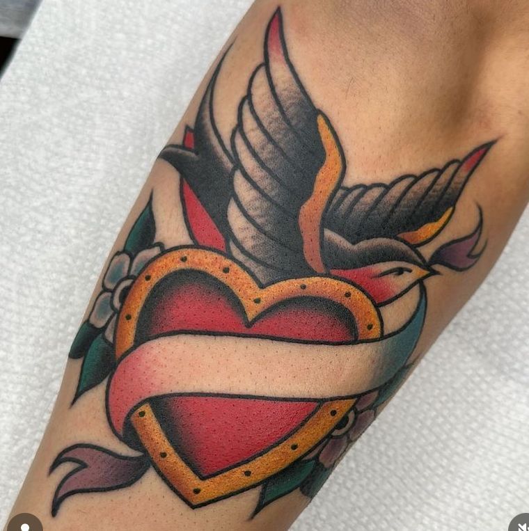 Heart with a bird and wings tattoo in red, teal, and black on skin