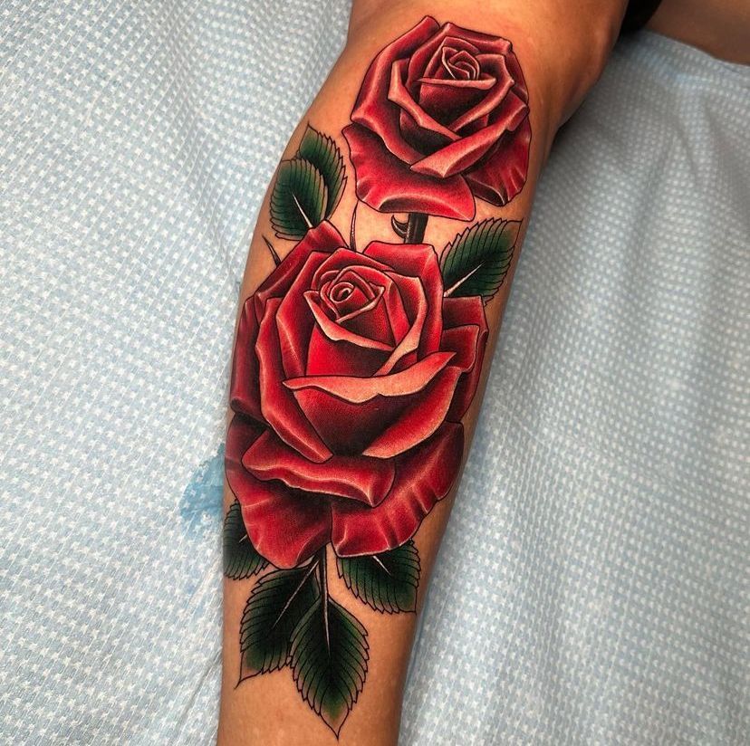 Forearm tattoo of two red roses with green leaves on a light blue background