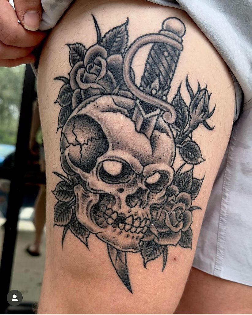 Black-and-gray skull tattoo with roses and a dagger on an upper arm