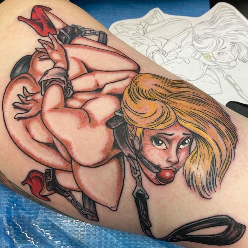 Tattoo of a red-heeled woman with blond hair curled into a ball on skin, with a faint sketch beside it