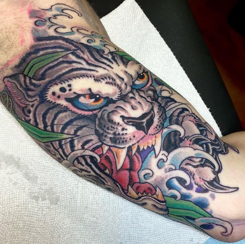 Colorful tiger tattoo on a forearm, with a snarling face and floral details on white fabric.