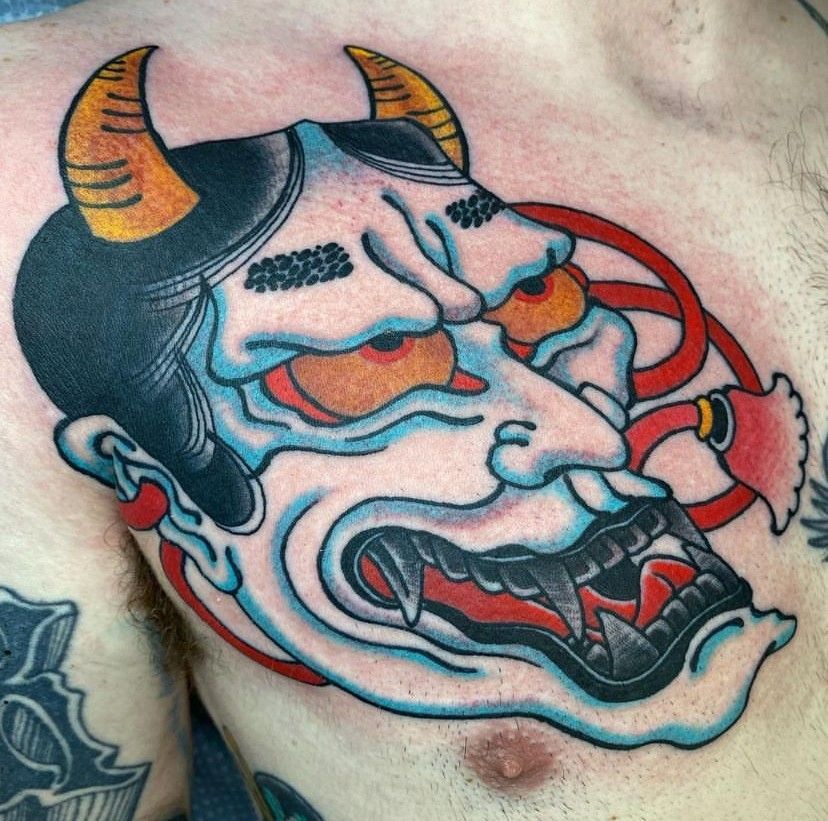Colorful oni mask tattoo with orange horns and red accents on skin