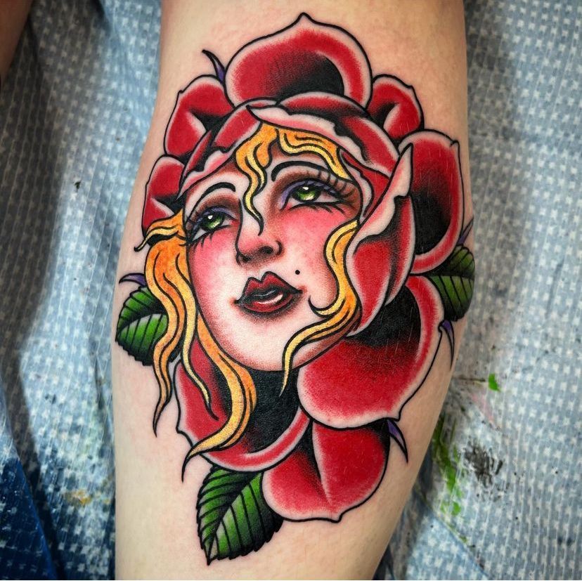 Colorful tattoo of a woman’s face framed by red rose petals and green leaves on skin