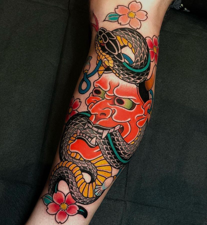 Colorful snake and red oni tattoo on a forearm with pink flowers