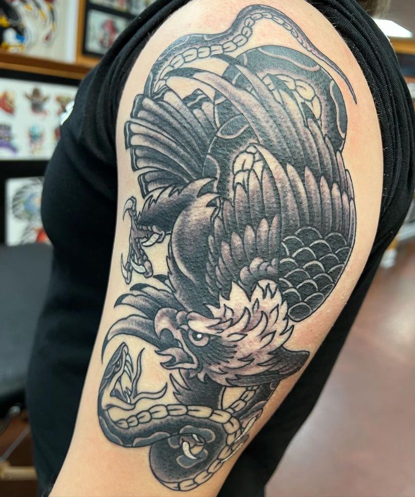 Black-and-gray dragon tattoo covering an upper arm in a tattoo studio