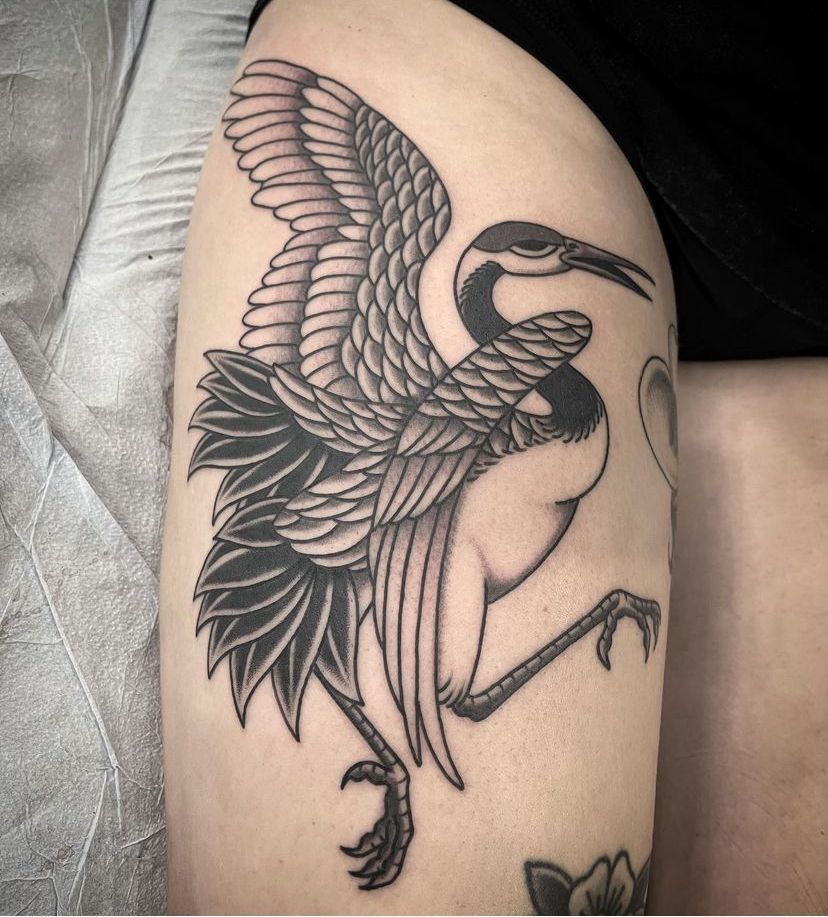 Black-and-gray crane tattoo on a person’s thigh, shown in close-up.