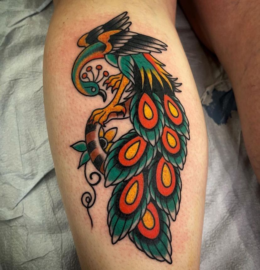 Colorful peacock tattoo on a person’s thigh, with teal, orange, and red feathers.