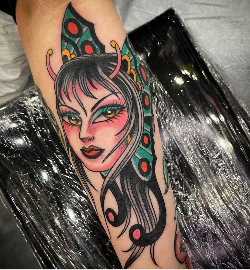 Colorful tattoo of a stylized face with pink eyeshadow, black hair, and green-red decorative shapes on a leg